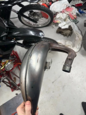 Technigas krök derbi - Säljer en metallfärgad avgaskrök med böjd form, passar till cross eller moped. Tillverkad i metall och har fäste för montering. Perfekt för dig som vill byta eller uppgradera avgassystemet.