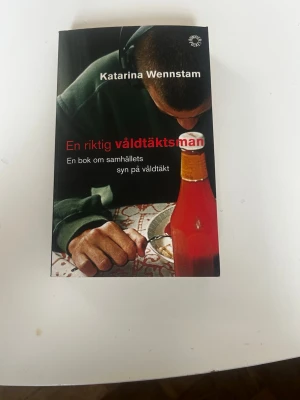 En riktig våldtäktsman av Wennstam - En pocketbok av Katarina Wennstam med svart omslag och röd text. Boken handlar om samhällets syn på våldtäkt och innehåller intervjuer och analyser kring ämnet. Omslaget visar en person i grön tröja och en röd glasflaska på ett bord.