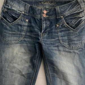 Snygga y2k blåa jeans  - Snygga blå jeans med slitningar och stora fickor både fram och bak. Jeansen har dubbla kopparfärgade knappar och coola sömdetaljer. 