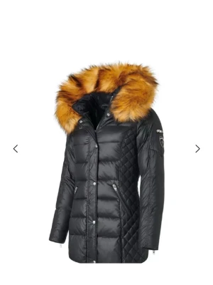 Svart dunjacka med fuskpäls från Rockandblue - Snygg svart dunjacka från Rockandblue med stor huva och lyxig fuskpäls i orange-bruna toner. Jackan har quiltade partier på sidorna, dragkedjor vid fickorna och Rockandblue-logga på ärmen. Perfekt för kalla vinterdagar och riktigt trendig look.  Finns i Luleå! 