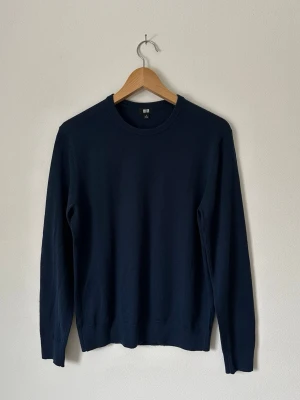 Mörkblå stickad tröja från Uniqlo - En stilren mörkblå stickad tröja från Uniqlo med rund halsringning och långa ärmar. Tröjan har en klassisk passform och är tillverkad i ett mjukt, tunt material som passar perfekt till lager-på-lager. Enkel design utan mönster för en clean look. 8B4