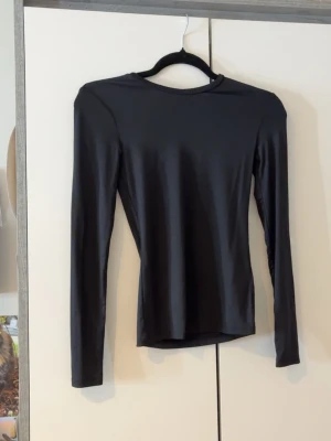 Svart långärmad topp från H&M - En stilren svart långärmad topp från H&M i stretchigt material. Toppen har en enkel, rund halsringning och en tight passform som sitter snyggt på kroppen. Perfekt att matcha med jeans eller kjol för en clean look.