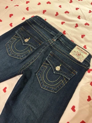 Mörkblå True Religion jeans - Säljer ett par mörkblå bootcut jeans från True Religion i storleken 26 där benen är uppsydda men inget som syns från utsidan🥰 har använd dem ungefär 2 gånger men känner att det inte är riktigt min stil. Innebenslängd: 81cm
