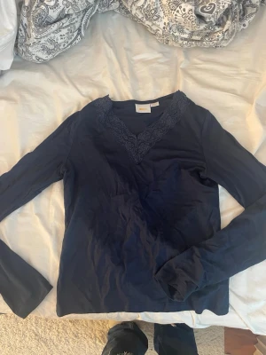 Mörkblå långärmad topp med spets - Snygg mörkblå långärmad topp från Gina Tricot med v-ringning och dekorativ spetsdetalj runt halsen. Säljer toppen för att den är för liten!💝
