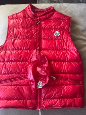 Moncler Gui Röd - Säljer min röda Moncler gui då den tyvärr inte får den kärleken den förtjänar. Snålt använd så väldigt bra skick på den. OG som följer med är den lilla påsen man kan lägga västen i. Pris är ej hugget i sten 