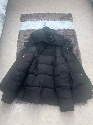 Svart dunjacka från Canada Goose - Säljer en svart dunjacka från Canada Goose med stor huva och rejäla kanaler fyllda med dun. Jackan har dragkedja, tryckknappar och detaljer som ger en klassisk vinterlook. Perfekt för kalla dagar och riktigt varm. Drag kedja har gått av men har fortfarande kvar den om ni vill fixa det själva arnnas har den tryckknappar 
