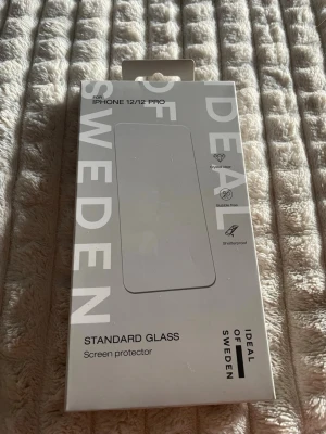 iDeal of Sweden skärmskydd i glas - Helt oöppnat! Säljer ett standard glass skärmskydd från iDeal of Sweden till iPhone 12/12 Pro. Skärmskyddet är genomskinligt och tillverkat i tåligt glas som är både kristallklart, bubbelfritt och splittersäkert. Perfekt för dig som vill skydda din mobilskärm utan att tumma på känslan.