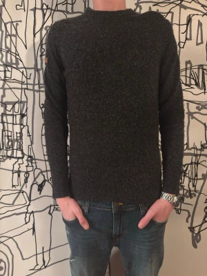 stickad Superdry tröja  - Mysig mörkgrå stickad tröja från Fjällräven med rund halsringning och ribbade muddar vid ärmslut och nederkant. Tröjan har en klassisk, enkel design och är tillverkad i ett grovt stickat material som passar perfekt till kalla dagar.