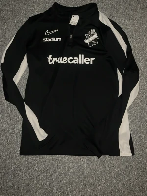 Träningströja AIK - Svart långärmad träningströja från Nike med AIK-logga på bröstet och vita detaljer längs ärmarna. Tröjan har halv dragkedja, Dri-FIT material och tryckta loggor från Stadium och Truecaller. Perfekt för fotbollsträning eller sport. Tröjan är storlek 158-170 inte 122-128 som det står på taggen. Har du några frågor är det bara att skriva🙌
