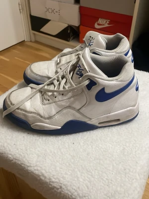 Nike Air Flight blå & vit - Nike Air Flight sneakers i vitt och blått med klassisk retrodesign. Skorna har en hög siluett, blå swoosh och detaljer, samt vadderad plös och krage. Ovandelen är i läder och mesh för både stil och komfort. Perfekta för dig som gillar old school vibes. Säljer för de inte passar mig längre.
