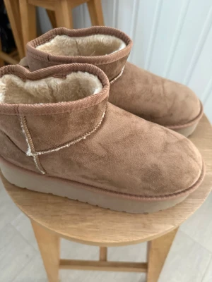 Bruna uggs - Mysiga bruna uggs från 157 med mjukt, ljust foder och mockaliknande utsida. Platform uggs. Skorna har en rund tå, låg skaft och synliga sömmar för en avslappnad look. Perfekta för kalla dagar när du vill hålla fötterna varma och bekväma. Har aldrig använt då de är för stora. 