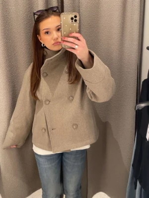 Beige kappa med hög hals - Skitsnygg kappa med dubbelknäppning framtill och hög krage. Storlek xs oanvänd från Gina tricot 