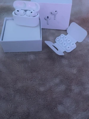 Apple AirPods Pro 3 - Säljer ett par vita Apple AirPods Pro med tillhörande laddningsetui och extra silikonpluppar i olika storlekar. Hörlurarna har en stilren och kompakt design, tillverkade i blankt plastmaterial. Perfekt för dig som vill ha trådlösa in-ear hörlurar med bra ljud och smidig användning.