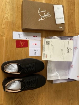 Svarta sneakers från Christian Louboutin - Stilrena svarta sneakers från Christian Louboutin med klassisk röd sula och diskret logga på sidan. Skorna har svarta skosnören, låg profil och är tillverkade i mocka med läderdetaljer. Perfekta för dig som vill ha en lyxig och tidlös look.