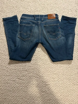 Blå Replay anbass slim fit jeans  - Säljer ett par blå jeans från Replay med slim passform och klassisk femficksdesign. Jeansen har snygga fades framtill och bakfickor med dekorativa sömmar. Märkespatch i läder bak i midjan. Perfekta för en avslappnad stil. Storlek 32/32
