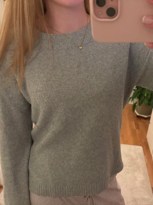 Ljusgrå stickad tröja - Mysig ljusgrå stickad tröja med rund halsringning och långa ärmar. Tröjan har en enkel och stilren design med ribbade muddar vid ärmslut och nederkant. Perfekt för lager-på-lager och passar till det mesta.