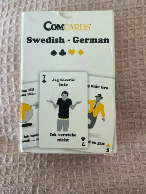 ComCards Swedish-German kortlek - En kortlek från ComCards med svenska och tyska fraser samt illustrationer. Perfekt för att lära sig språk på ett roligt sätt. Kortleken är vit med svarta och gula detaljer och innehåller både text och bilder på varje kort.