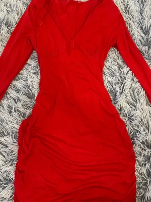 Röd långärmad festklänning - Snygg röd klänning med långa ärmar och omlottdetalj vid bysten. Klänningen har lätt scrunch som formar kroppen fint och en figurnära passform som framhäver siluetten. Perfekt för dig som vill sticka ut med en färgstark look. Passar både s och m