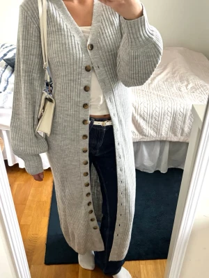 Lång grå ribbat kofta  - Lång, ribbstickad kofta i ljusgrått med bruna knappar hela vägen framtill. Kan även användas som klänning💗Obs: köpt från vinted så orsäker på märke! 
