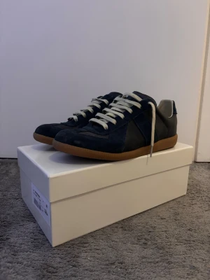 Maison Margiela skor - Säljer mina blå Maison Margiela skor då jag är intresserad av ett annat par. Perfekt nu till våren och sommaren!Skorna har en liten defekt därav är priset sänkt. Det är längst fram på skon som det har blivit blöt och fått lite mörkare färg. Skriv om det finns funderingar😊