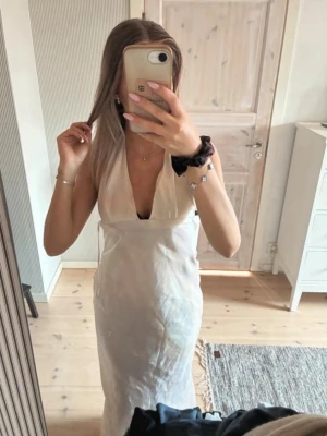 Beige balklänning  - Pris kan diskuteras vid snabb affär! Säljer en elegant vit långklänning med djup v-ringning och ärmlös design. Klänningen har en figurnära passform och är tillverkad i ett lätt, mjukt material som ger en lyxig känsla. Perfekt för dig som vill ha en stilren och trendig look.
