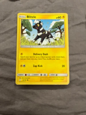 Pokémonkort Blitzle gul - Pokémonkort med motiv av Blitzle. Kortet har en gul ram och färgglad illustration med Blitzle i en grönskande miljö. Text och symboler i svart och vitt, samt detaljer om attackerna Delivery Dash och Zap Kick.