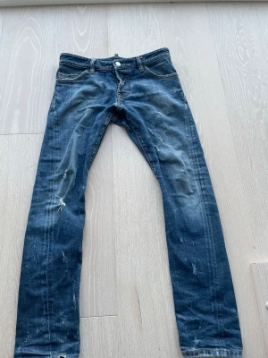 Blå slim fit jeans från Dsquared  - Säljer ett par blå slim fit jeans från Diesel med slitna detaljer och snygg tvätt. Jeansen har klassisk femficksdesign, gylf med knapp och dragkedja samt kontrastsömmar. Perfekta för en avslappnad och trendig look.