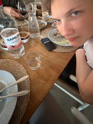 Ramlösa Granatäpple vattenflaska - (Lite drycken ur) Stor genomskinlig plastflaska med Ramlösa Granatäpple smaksatt vatten. Flaskan har röd och vit etikett och står på ett matbord tillsammans med glas och tallrikar.