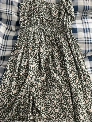 Grön blommig sommarklänning - Supersöt grön klänning med vitt och rosa blommönster. Smockad upptill och volangdetaljer vid axlarna. Perfekt för varma dagar och har en luftig, avslappnad passform. Klänningen är ärmlös och slutar ovanför knäna. För lite mindre barn finns ingen storlek eftersom den är köpt från Thailand 🇹🇭 men passar nån som  är 155 ungefär 😋♥️