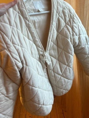 Quiltad offwhite cardiganjacka Zara - Quiltad cardiganjacka i offwhite från Zara. Jackan har ett knytband framtill, V-ringning och breda ärmar. Materialet är mjukt och vadderat med ett rutmönster. Perfekt för lager-på-lager.