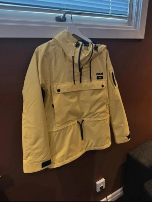 Gul skidjacka från Dope med huva - Snygg gul vindjacka från Dope med stor magficka, dragkedjor och svarta detaljer. Jackan har justerbar huva, kardborre vid ärmslut och praktisk ficka på ärmen. Perfekt för blåsiga dagar och streetstyle. Är i nyskick.