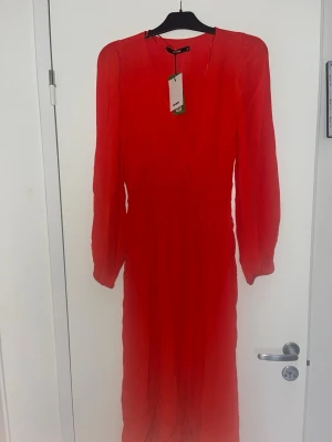 Röd långklänning med långa ärmar - Snygg röd långklänning med långa ärmar och rund halsringning. Klänningen har en enkel, elegant design och är tillverkad i ett lätt, flytande material som ger ett fint fall. Perfekt för dig som vill sticka ut med färg.