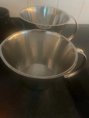 2x1L Måttkannor i Rostfritt Stål #1 - Två stycken måttkannor i rostfritt stål med handtag. Perfekta för att mäta upp vätskor eller ingredienser i köket. Klassisk konisk form och tydliga måttmarkeringar på insidan. Snygg och praktisk design som passar alla kök.