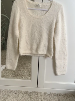 Vit fluffig stickad tröja H&M - Supermjuk och fluffig vit stickad tröja från H&M med rund halsringning och långa ärmar. Tröjan har en croppad passform och är perfekt för att skapa en mysig och trendig look. Materialet känns lätt och skönt mot huden.