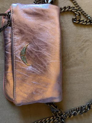 Rosa metallic axelväska från Zadig & Voltaire - Säljer min fina Mini väska från Zadig och Voltaire i liten storlek. Aldrig använd och supersöt och unik.🩷🌷den är som ny dustbag tillkommer givetvis äkta! Metallic färg i rosa lila med rosa kanter och turkos Zadig logga! Två olika band ett kortare och ett längre banden går att ta av.