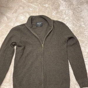 Olivgrön kofta med dragkedja Indicode - Säljer en olivgrön stickad kofta från Indicode i storlek medium. Koftan har hel dragkedja framtill, hög krage och långa ärmar. Perfekt för lager-på-lager och chill stil. Materialet är mjukt och ger en clean look. Den är oanvänd så 10/10 