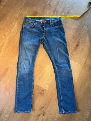 Nudie Jeans Grim tim - Säljer mina Nudie jeans, modell Grim Tim. Köpt i December 2025 använd fåtal gånger men blivit insydda i låren och även sytt fast en extra knapp i midjan!   Storlek 33/34 men blivit insydd i låren och midjan till 32/34  	•	Midja: ca 42,5 cm 	•	Innerben: ca 78–79 cm 	•	Ytterben: ca 103–104 cm 	•	Lårbredd: ca 24–25 cm  Måtten är ungefärliga (±1 cm)  Hojta vid eventuella frågor! 