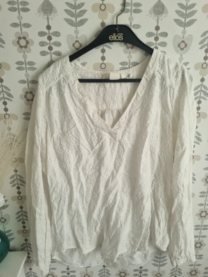 Vit v-ringad blus från H&M  - Säljer en vit blus från H&M med v-ringning och långärmad design. Blusen är tillverkad i ett lätt och krispigt material som ger en avslappnad look. Perfekt att matcha med jeans eller kjol för en stilren outfit.