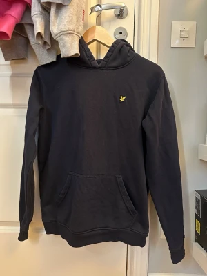 Mörkblå hoodie från Lyle & Scott - Snygg mörkblå hoodie från Lyle & Scott med klassisk gul logga på bröstet.
