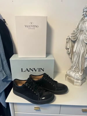 Svarta lackade sneakers från Lanvin - Snygga svarta sneakers från Lanvin i blankt lackmaterial med svarta skosnören och gummisula. Klassisk låg modell med rund tå och diskret design som passar till det mesta. Insidan är beige och ger en lyxig känsla.