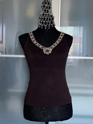 Svart linnetopp med pärldetaljer - Supersnygg svart linnetopp från Ricco Vero med v-ringning och pärlbroderier längs halsringningen. Har tyvärr blivit solblekt mitt på (se bild).