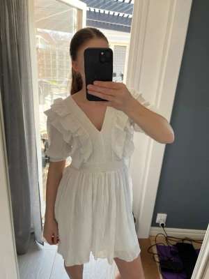 Vit volangklänning med v-ringning - Superfin vit kortklänning med v-ringning och volangdetaljer både fram och bak. Endast använd en gång 