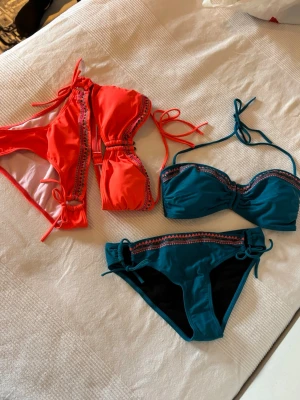 Två bikinis i turkos och orange - Säljer två snygga bikinis, en i turkos och en i korall. Båda har dekorativa band och fina detaljer längs kanterna. Den turkosa har bandeau-topp med knyt och matchande trosa, medan den korallfärgade har trekantsmodell med knyt i sidorna. Perfekta för stranden! Bikinierna är inte använda!
