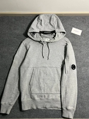 C.P. Company hoodie – size S - Selling a really clean C.P. Company hoodie in a nice grey color. Simple and easy to wear, with the signature lens detail on the sleeve that gives it that extra touch.  * Size: S * Length: 64 cm * Width (pit to pit): 53 cm  Condition is good overall – well taken care of, no major flaws. Still looks fresh and feels great on.  Perfect everyday hoodie that goes with pretty much anything.  Shipping available 📦 Message me if you’ve got any questions 👍