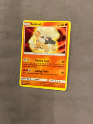 Pokémonkort Torkoal - Pokémonkort med Torkoal-motiv. Kortet har en färgstark design i orange, gul och svart med Torkoal i mitten och eldiga detaljer. Kortet är tillverkat av laminerad kartong och har text och illustration på framsidan.
