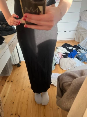 Svart långkjol i mjukt material - En svart, lång och rak kjol i mjukt och stretchigt material. Enkel och stilren design med resår i midjan som gör den bekväm att bära. Perfekt att styla med både sneakers och boots. Och slits där bak