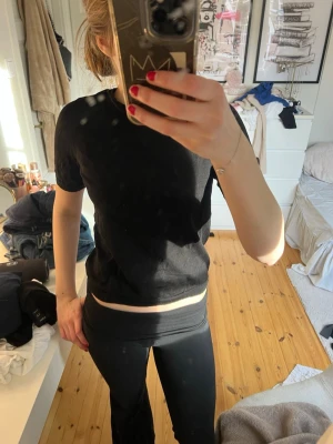 Svart t-shirt från Lindex - En klassisk svart t-shirt från Lindex med rund hals och korta ärmar. T-shirten har en enkel och stilren design, perfekt att matcha med allt. Materialet känns mjukt och bekvämt mot huden.