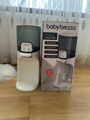 Baby Brezza Instant Warmer - Baby Brezza Instant Warmer är en vit och grå vattenvärmare för nappflaskor. Den har en stilren design med digitala knappar och genomskinlig vattentank. Perfekt för att snabbt värma vatten till modersmjölksersättning.