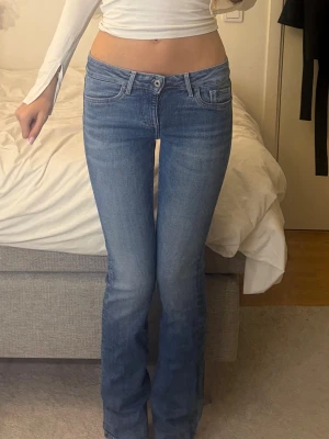 Blå bootcut jeans från Pepe Jeans - Säljer ett par klassiska blå bootcut jeans från Pepe Jeans i modellen picadilly. Jeansen har fem fickor, midwaist och en snygg tvätt med diskreta slitningar. Bakfickorna har en vågig detaljsöm och läderpatch i midjan. Perfekta för en trendig och avslappnad look.