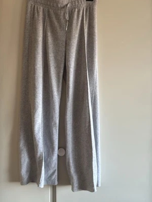 Grå vida mjukisbyxor med resår low rise - Grå mjukisbyxor med breda ben och resår i midjan samt dragsko. Byxorna är tillverkade i ett mjukt och stretchigt material som känns skönt mot huden. Perfekta för en avslappnad och chill stil.